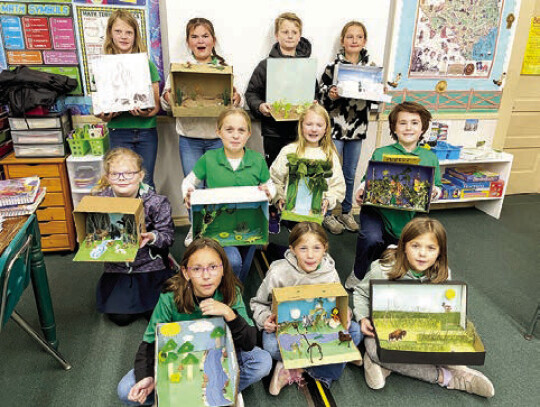 4th graders proudly show their biome projects in science class. The students from left in the front are Isabelle Marek, Lainey Melnar and Lillie Herzik. In the middle row from left are Faith Vavra, Charlee Davis, Hadley Brandt and Patrick Baggerly. In the back row from left are Kelsey Weid...