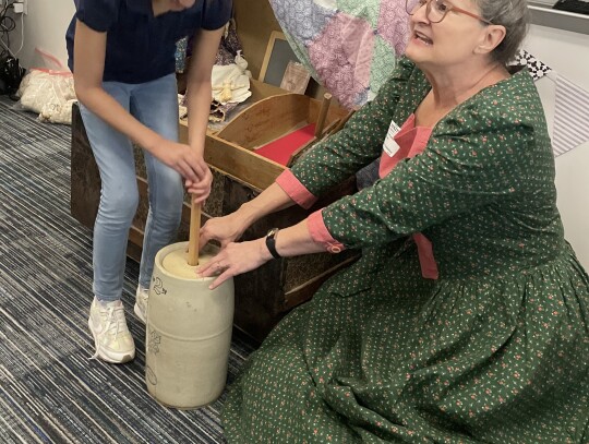 Donna Pustejovsky of the Daughters of the Republic of Texas shows SAS 4th grader Kate Crosby how butter was churned.