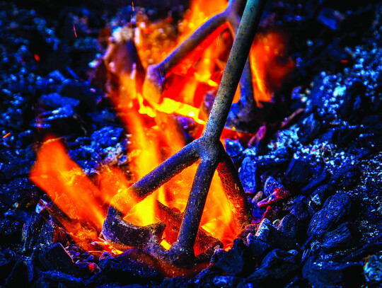 Hot coals in a fire heat a branding iron. Adobe Stock photo